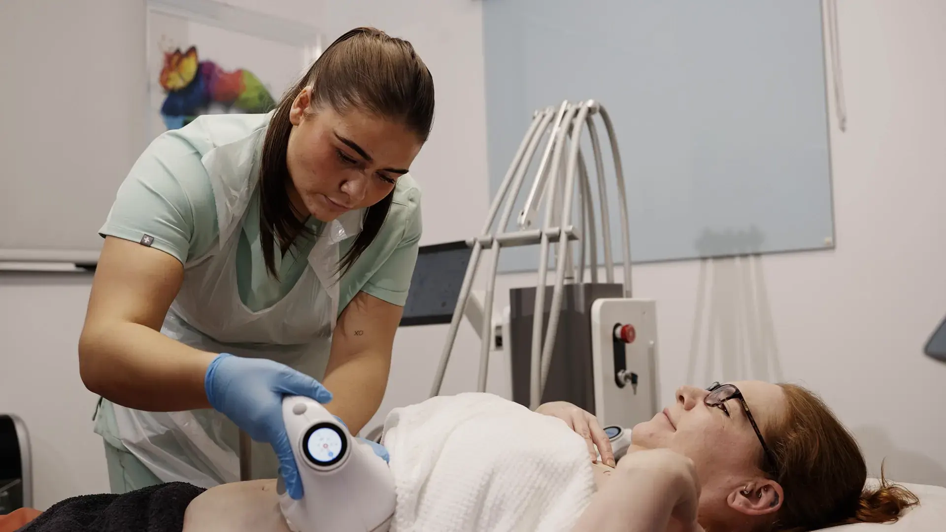 A practitioner treats a client's abdomen with a cavitation handpiece in a treatment room