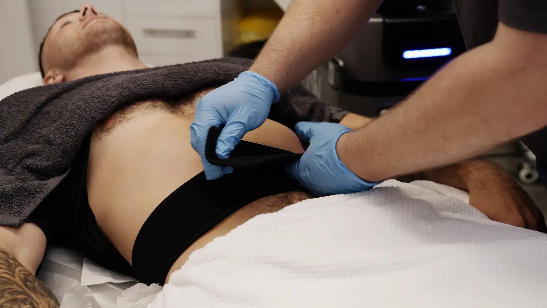 Two practitioners position a strapped applicator on a client's abdomen