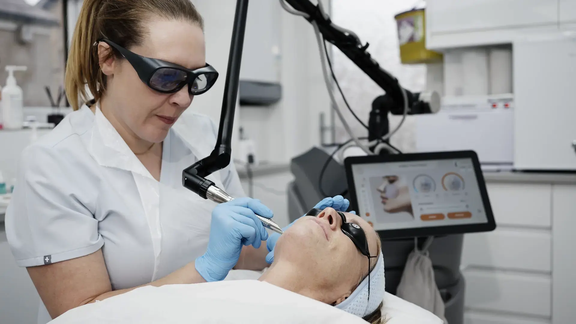 A practitioner in protective glasses treats a client's face with an erbium laser handpiece