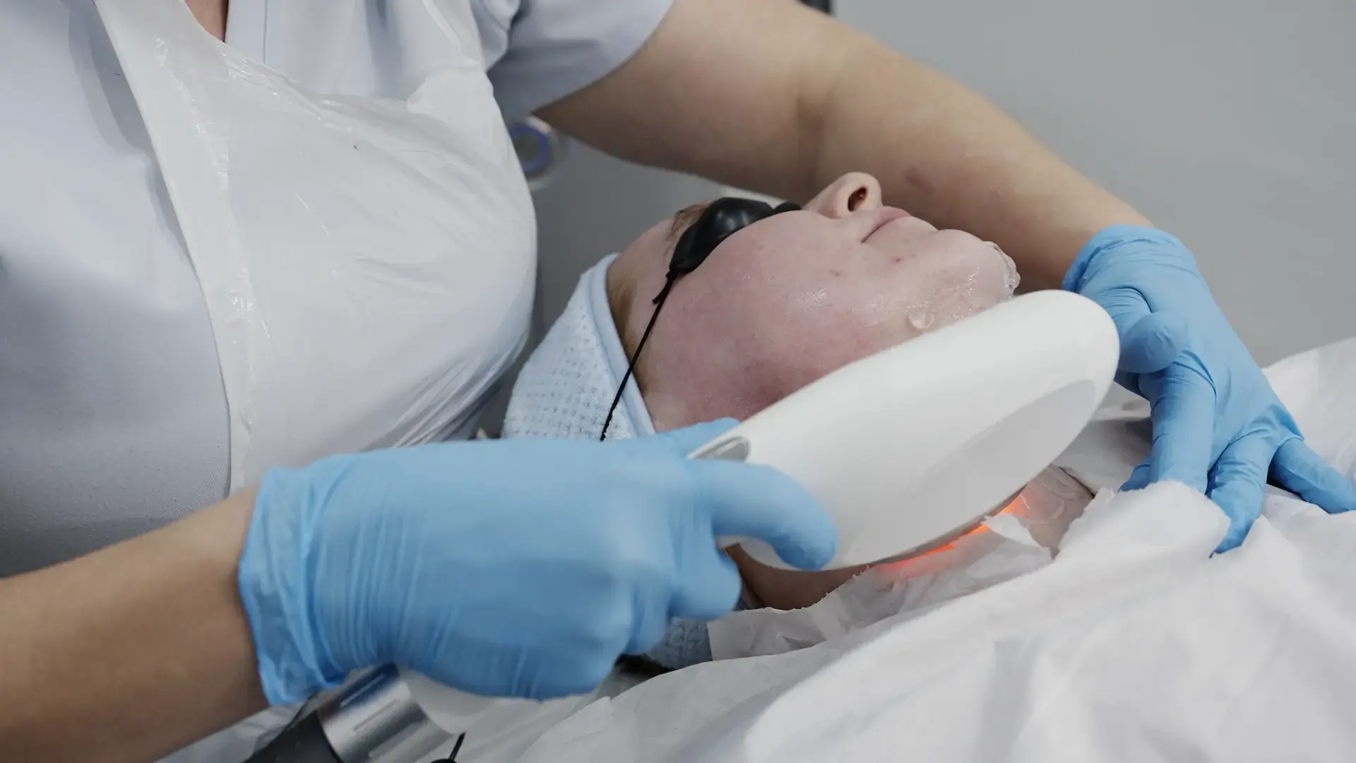 A practitioner glides a white handpiece along a client's jawline with a red glow beneath