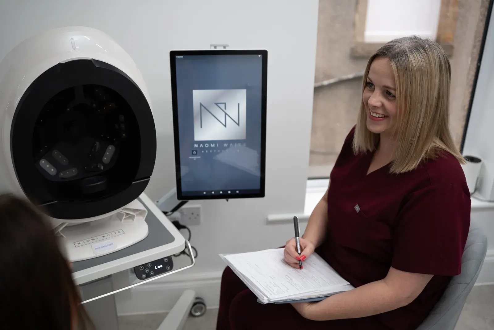 A practitioner takes notes during a consultation beside the skin analyser