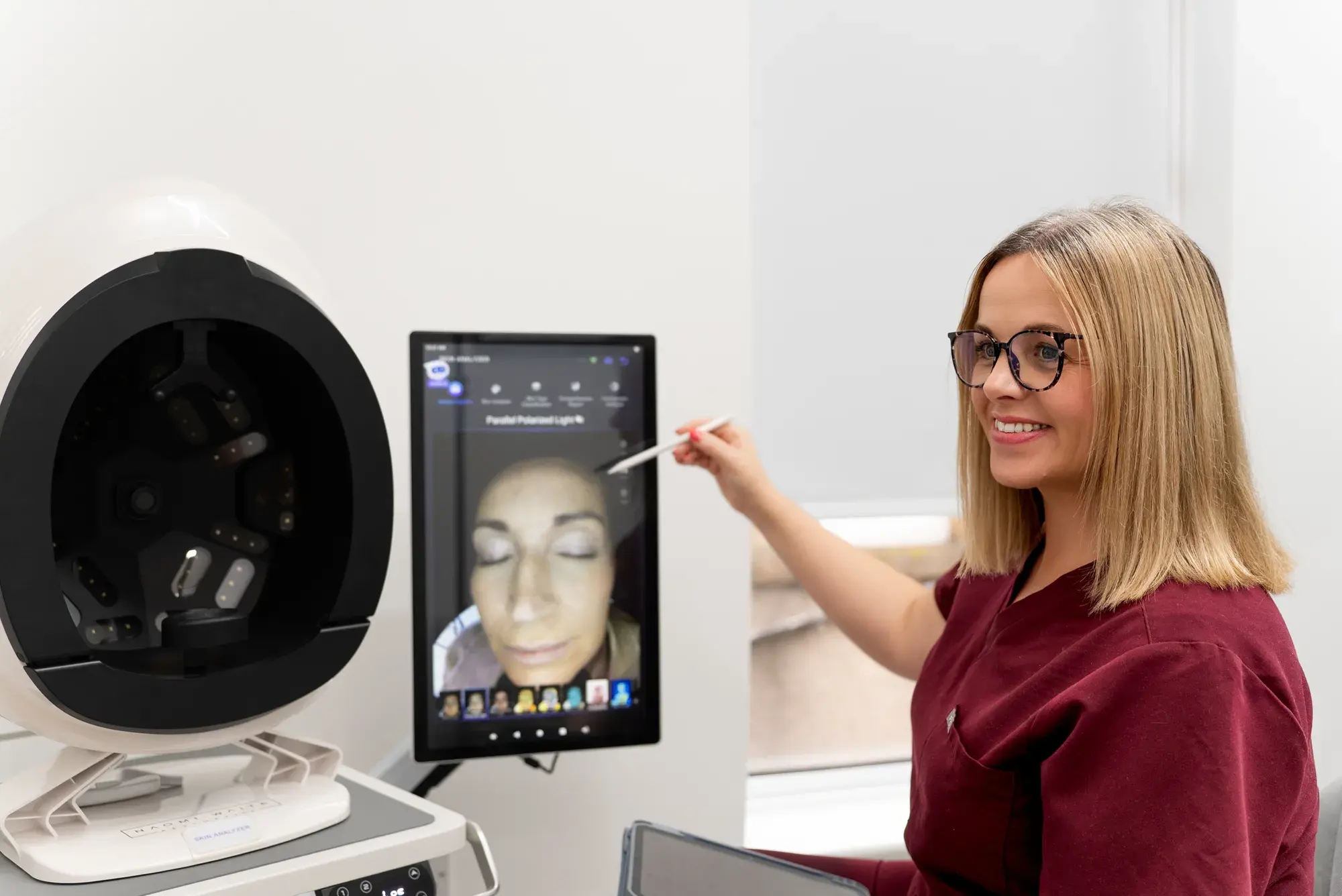 A practitioner stands beside a skin analysis mirror and screen showing a client's face
