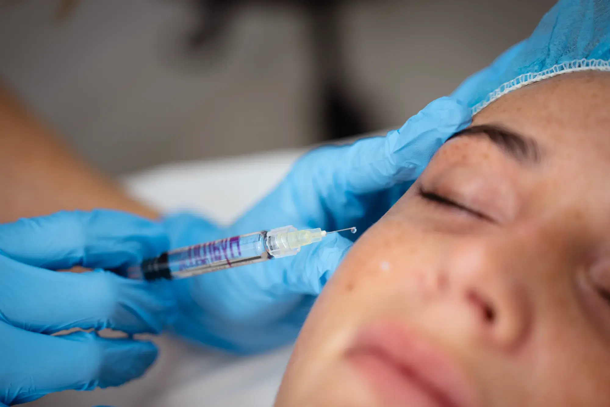 A gloved hand holds a syringe against a client's cheek