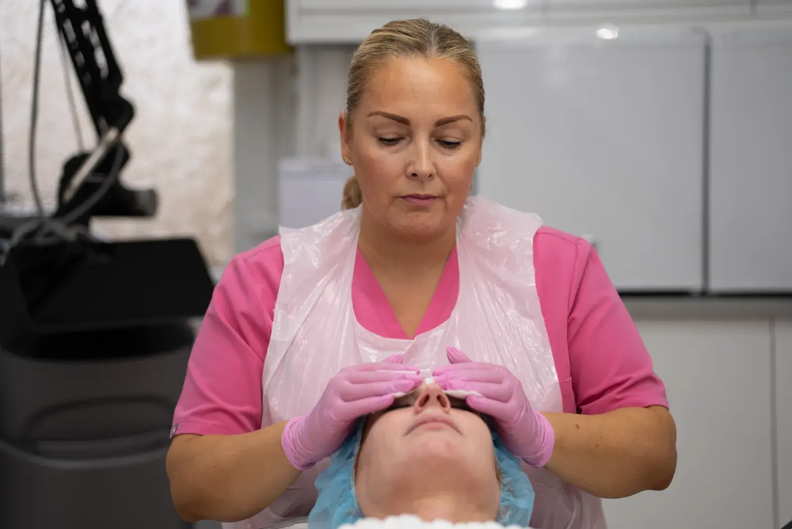 A practitioner in a pink tunic massages a client's face during a facial