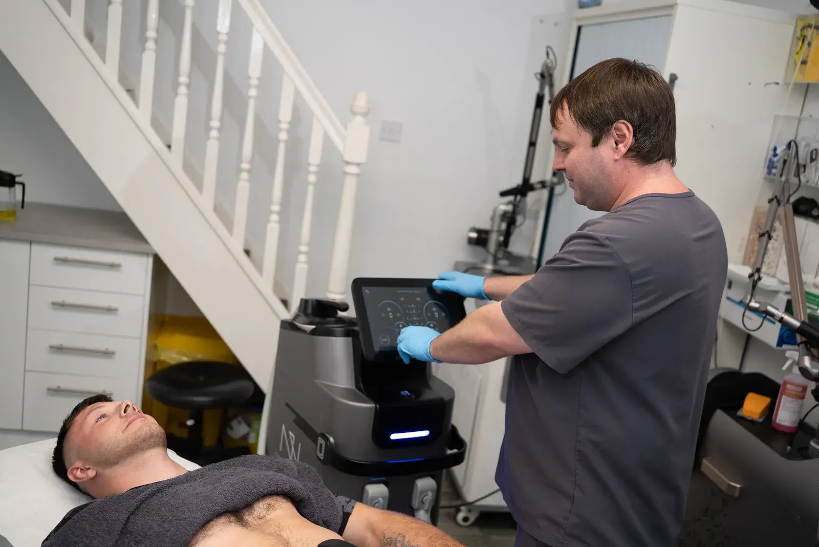 A practitioner adjusts the muscle toning machine while a client lies on the couch