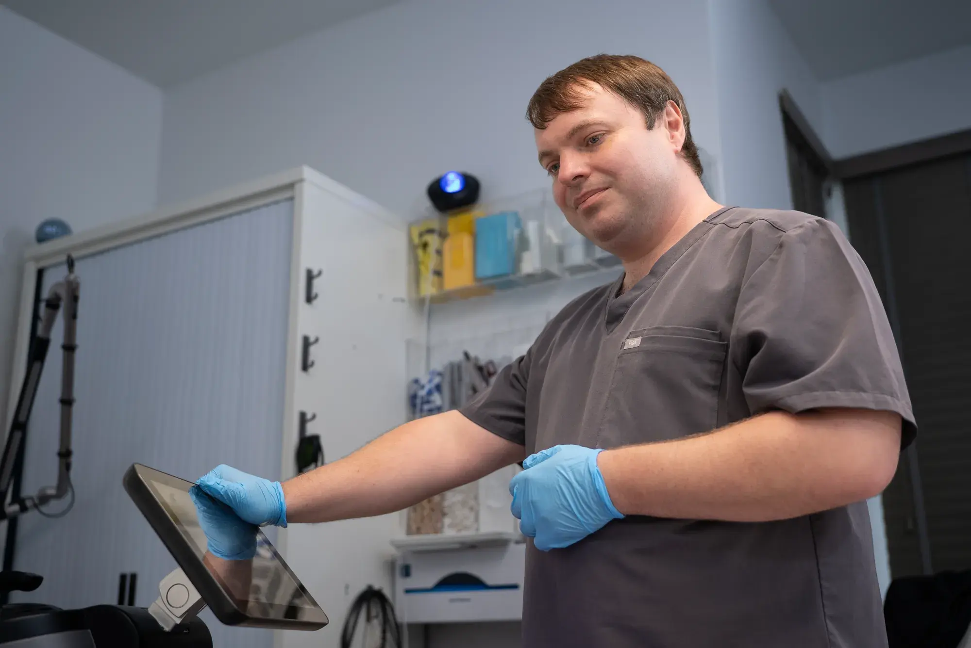 A practitioner in a grey tunic looks at a tablet beside a treatment couch