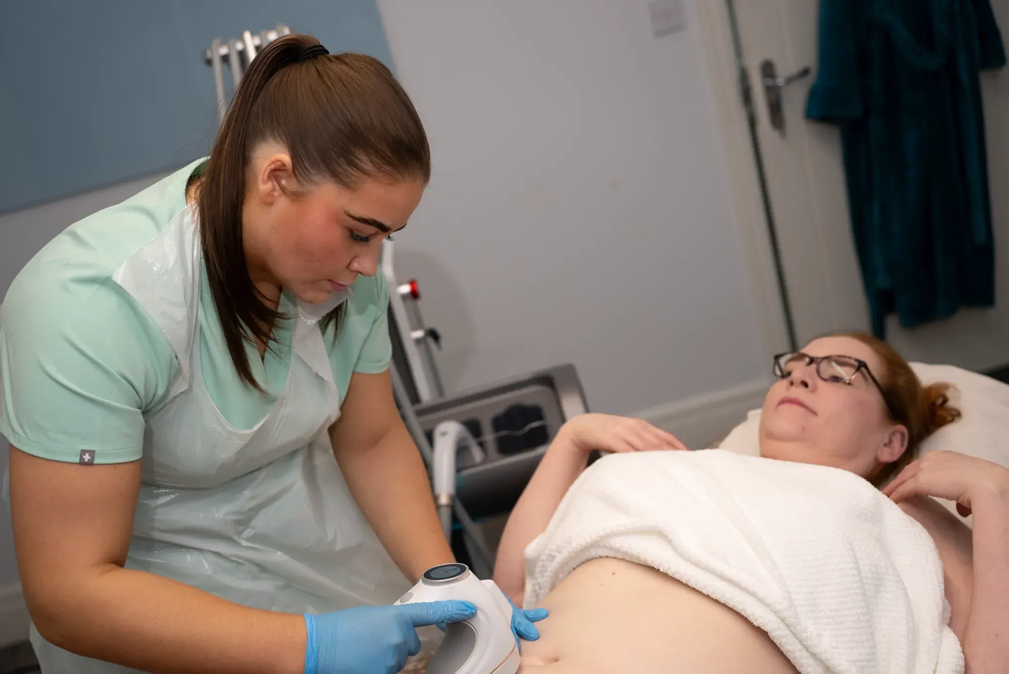 A practitioner in a green tunic treats a client's abdomen as the client lies back
