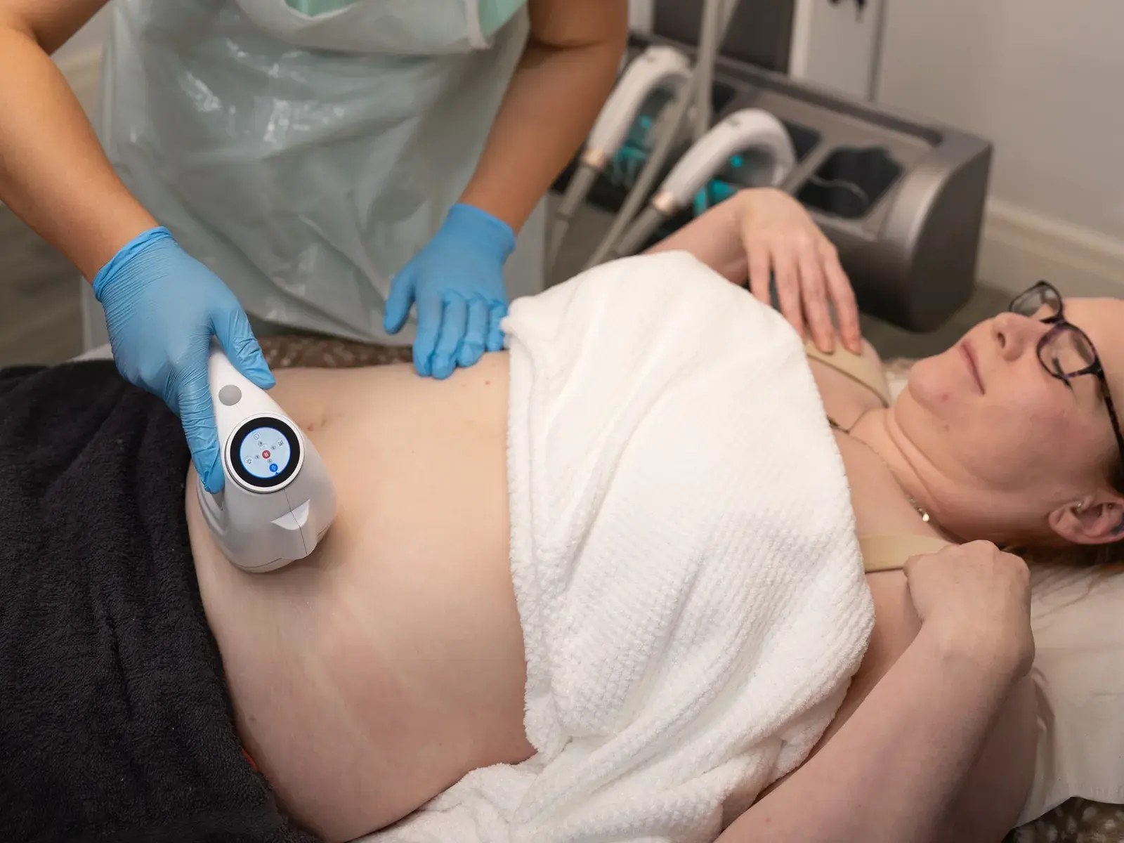 A cavitation handpiece held against a client's abdomen as she lies on a couch