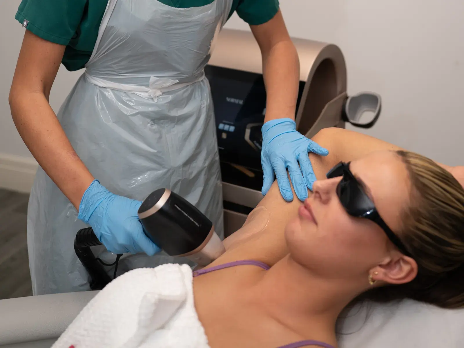 A practitioner in protective glasses treats a client's underarm with a diode laser handpiece