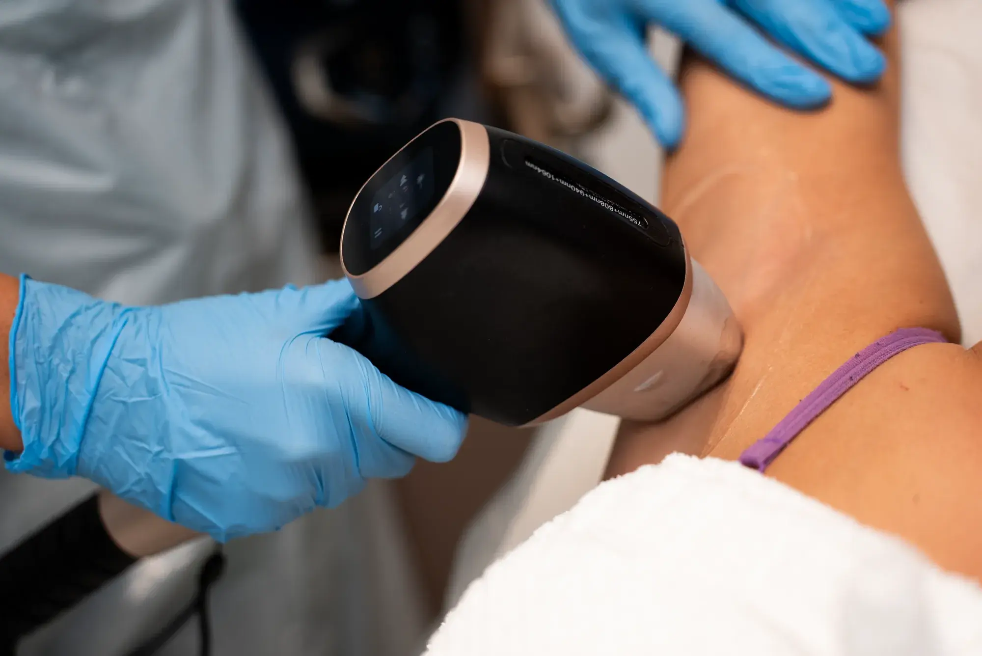 A gloved hand holds a diode laser handpiece against a client's neck