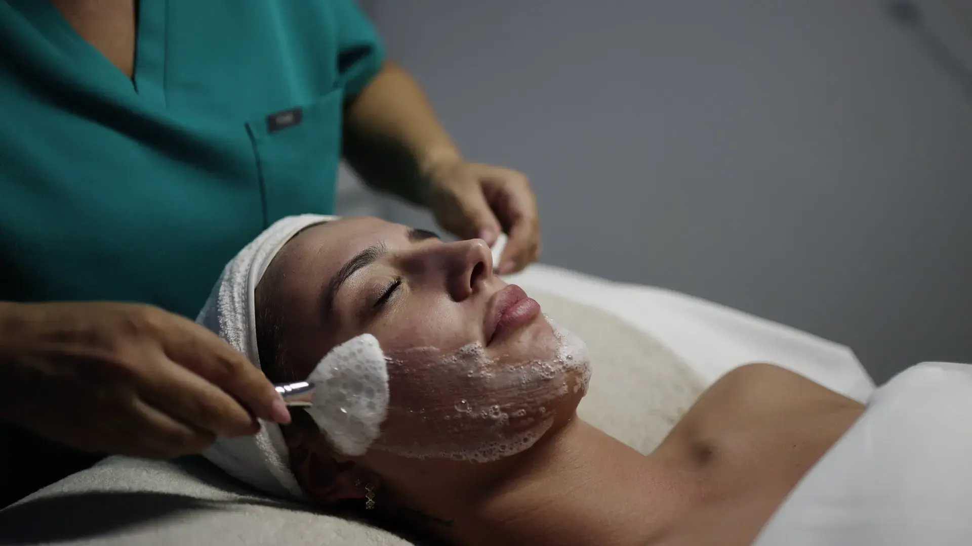 A practitioner brushes a pale product onto a client's face