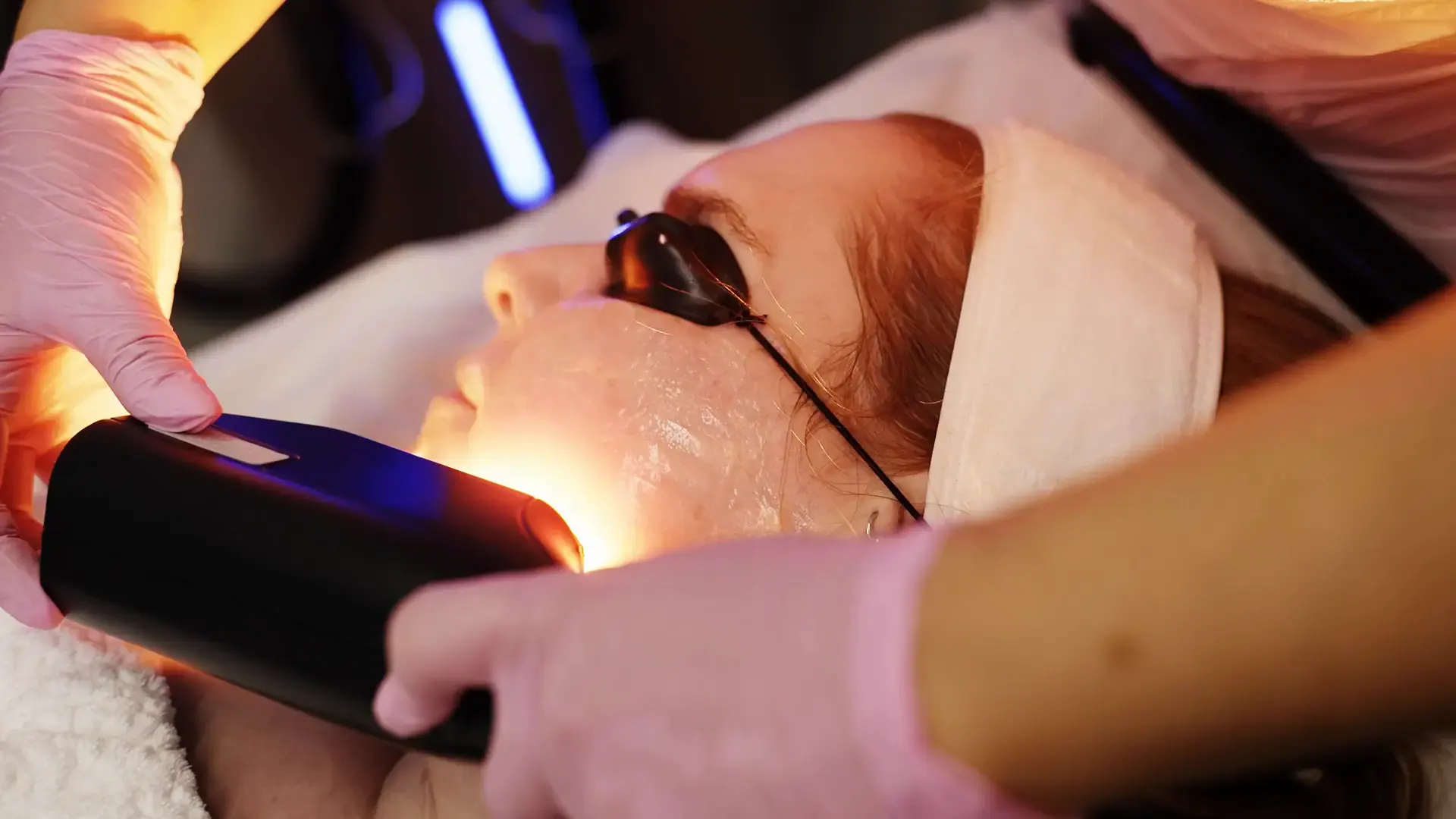 A warm orange light from a handpiece held close to a client's face while they wear eye protection