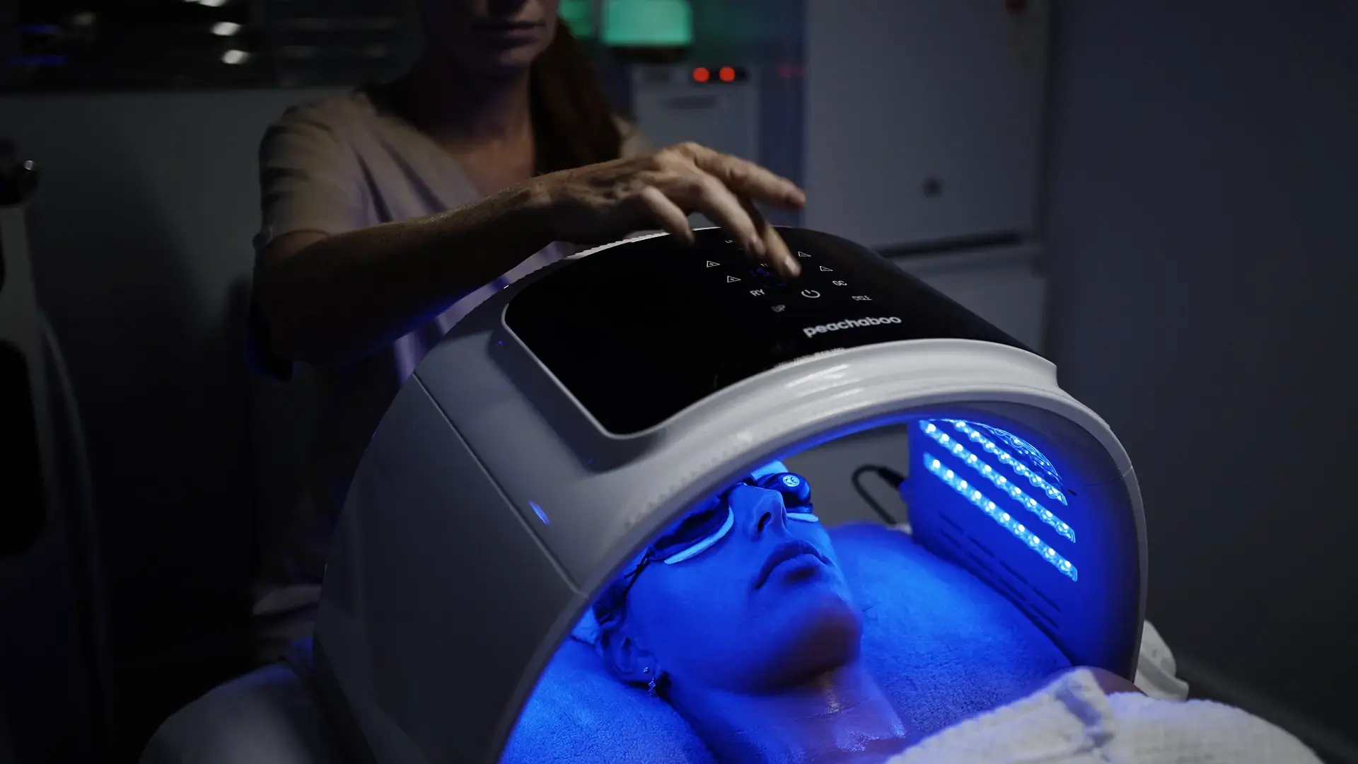 A client lies beneath a blue light dome while a practitioner stands beside the couch