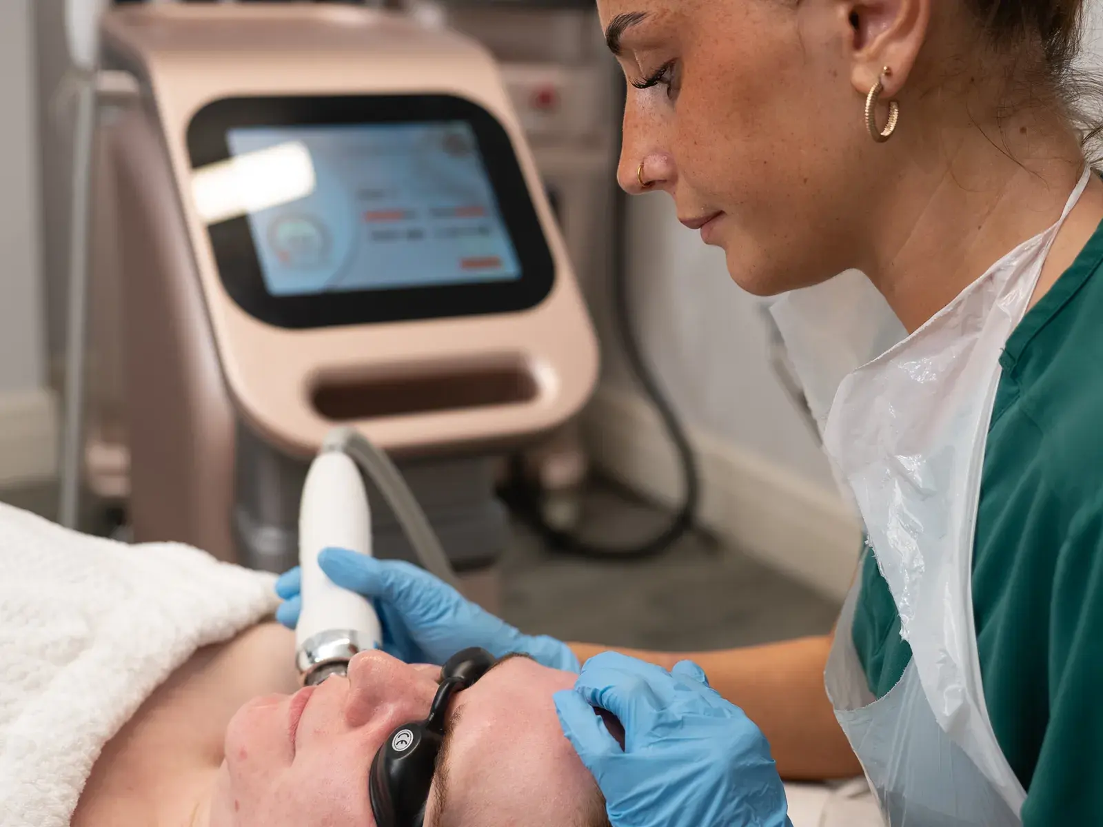 A practitioner in a green tunic treats a client's face beside the radio frequency machine